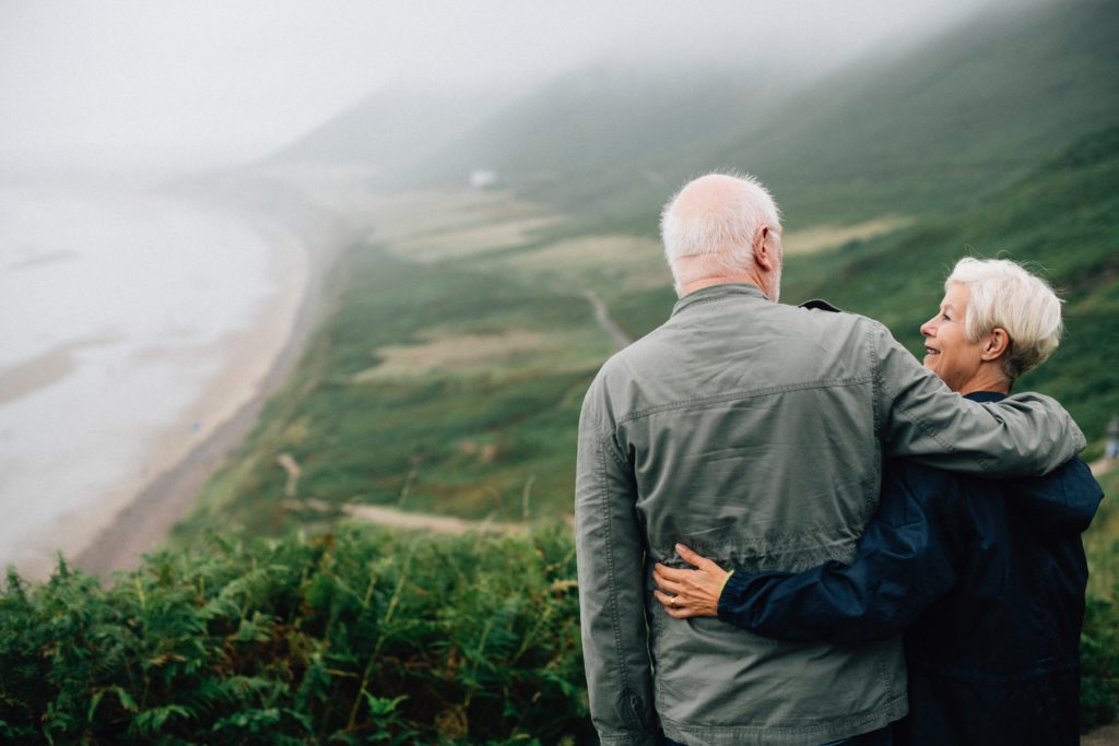 Image: An older couple hugs, looking down on the coastline. Learn how our estate appraisal services can help you plan for your future.
