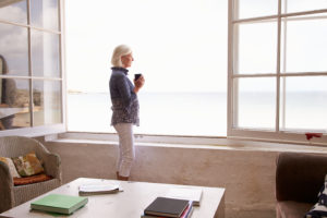 A woman holds a coffee cup and stares peacefully out a window. Learn how appraisals help with divorce settlements.